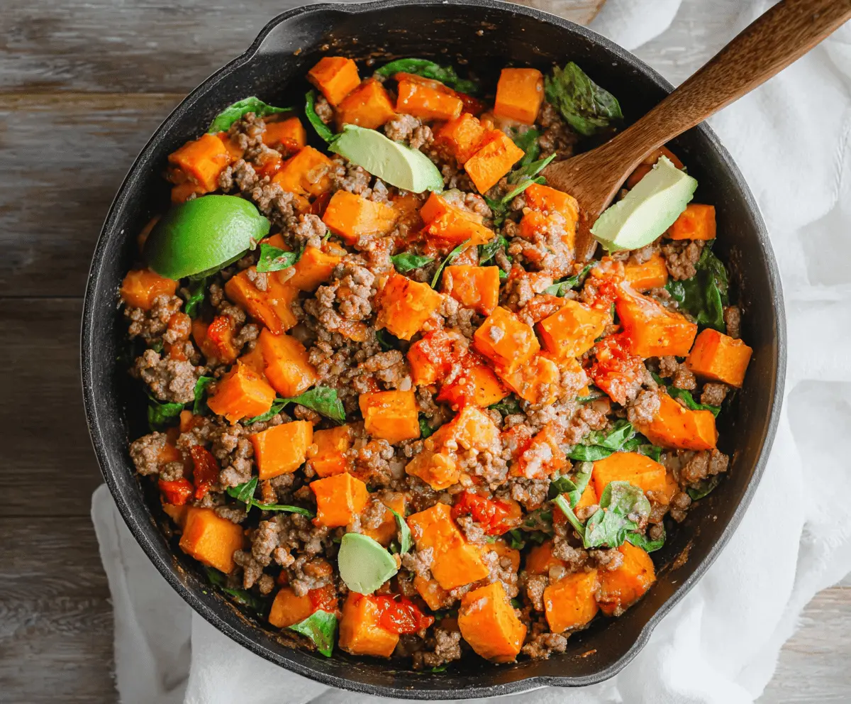 Delicious sweet potato and ground beef skillet topped with fresh herbs, served in a rustic skillet for a hearty and healthy meal.