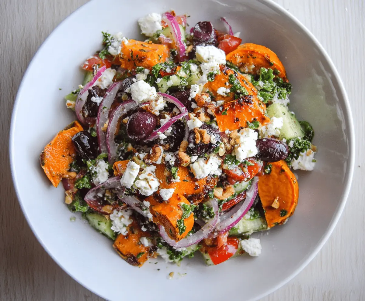 Colorful sweet potato Greek salad with cherry tomatoes, cucumber, red onion, Kalamata olives, feta cheese, and fresh herbs in a bowl