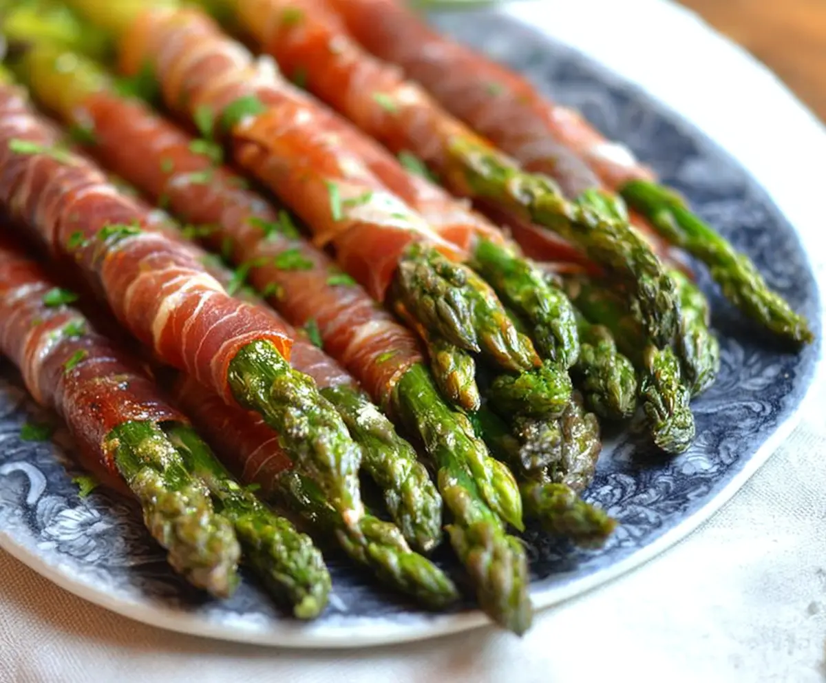 Delicious prosciutto-wrapped asparagus spears on a white plate, perfect for appetizers or snacks.
