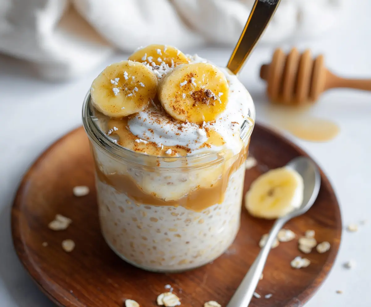 Banana cream pie flavored protein overnight oats in a jar with fresh bananas and whipped cream topping.