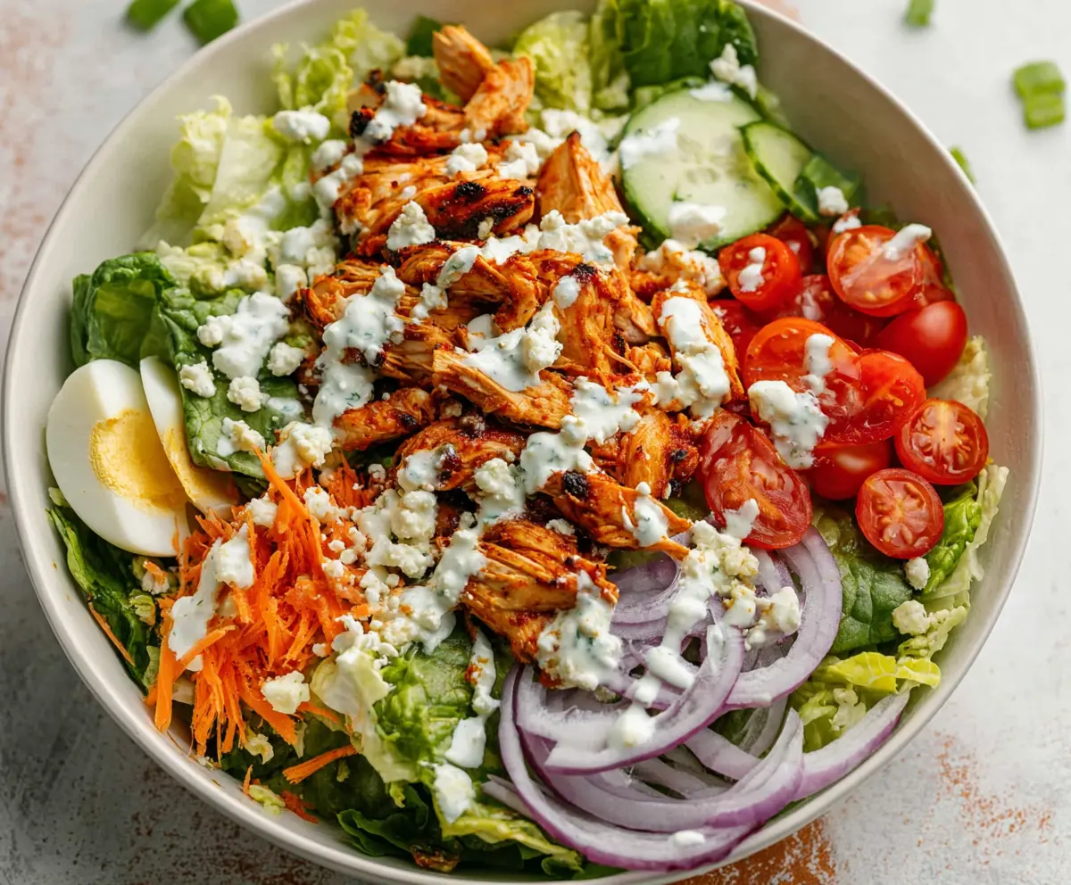 Buffalo chicken salad with fresh greens, celery, and blue cheese crumbles on a white plate