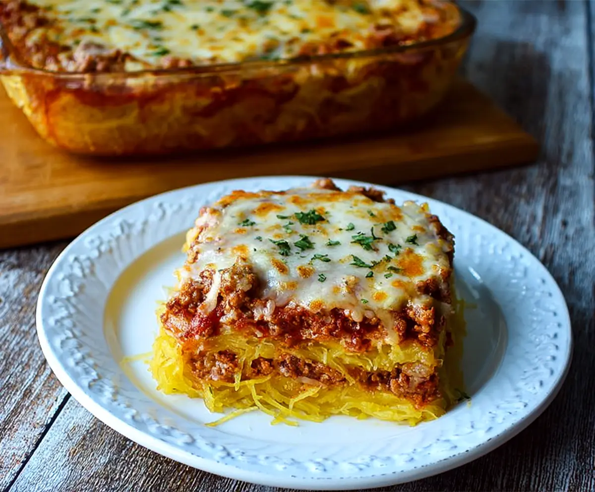 Baked spaghetti squash lasagna layered with marinara sauce, cheese, and fresh herbs on a white plate.
