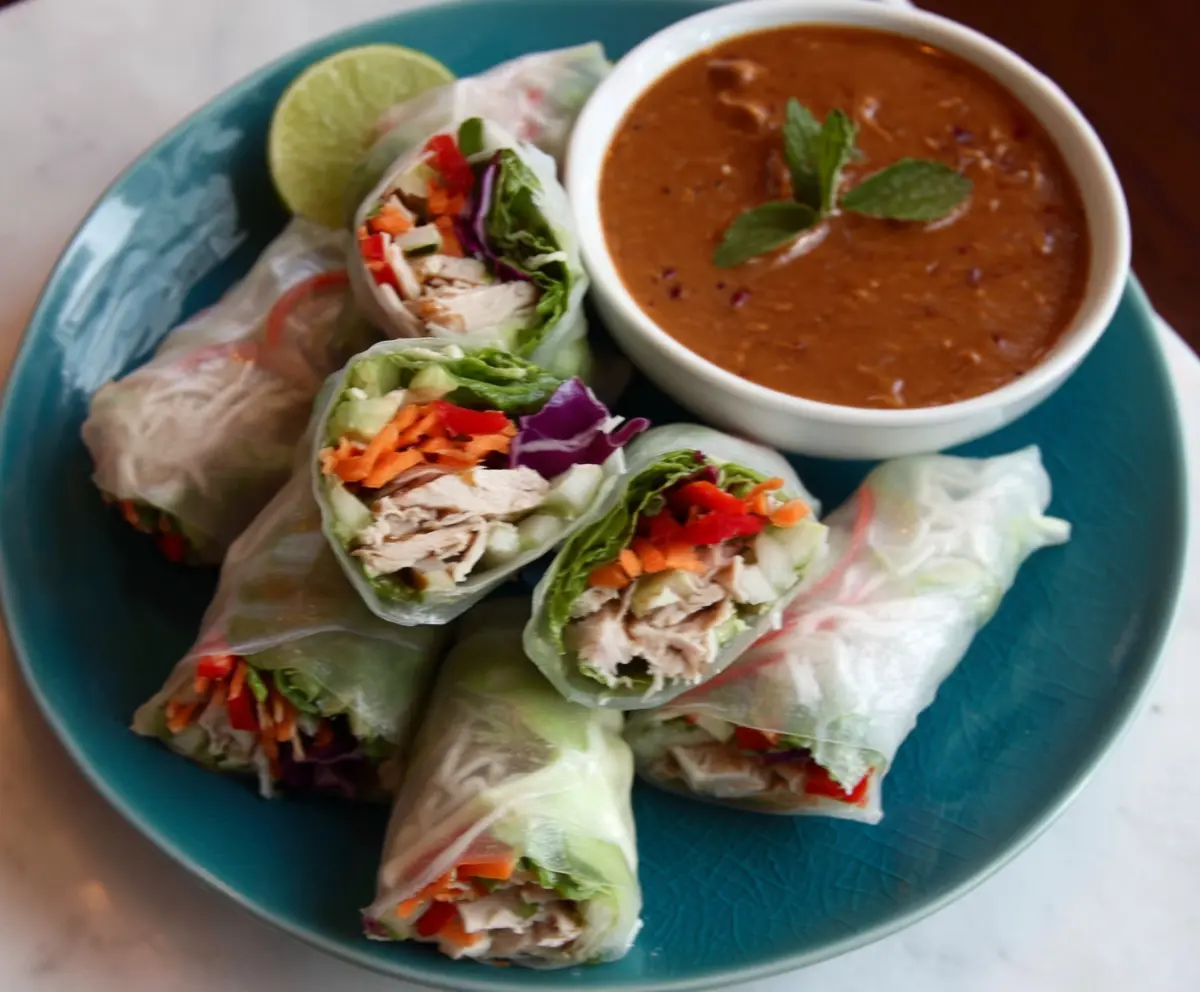 Crispy pork spring rolls served with a tangy peanut lime dipping sauce on a white plate.